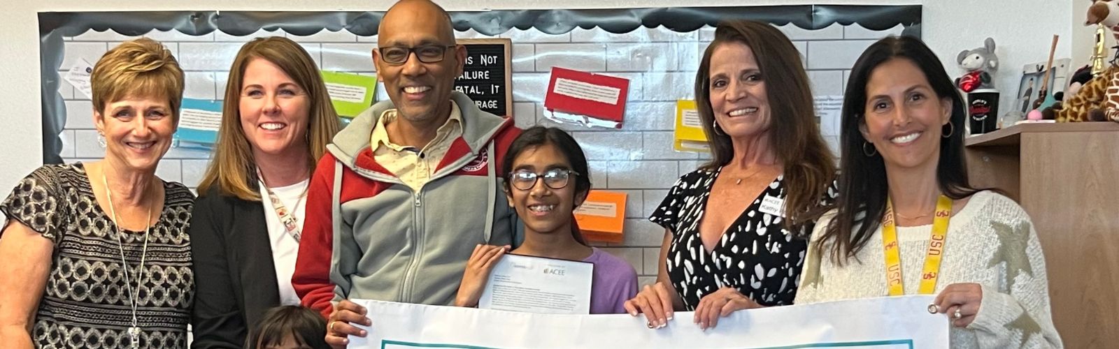 Photo of a student holding an essay with her family and teacher.