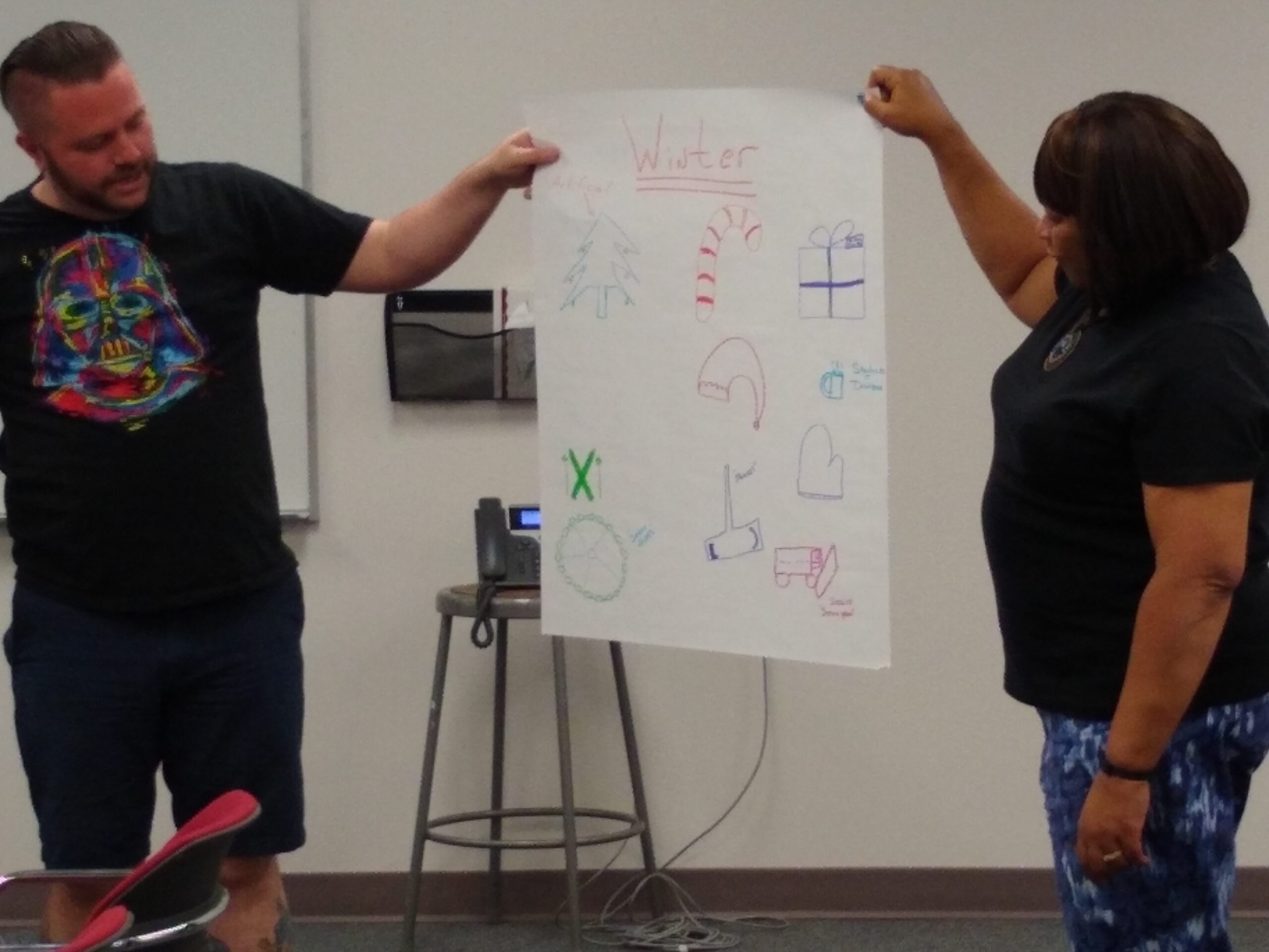 Two teachers holding up a poster paper with drawings.