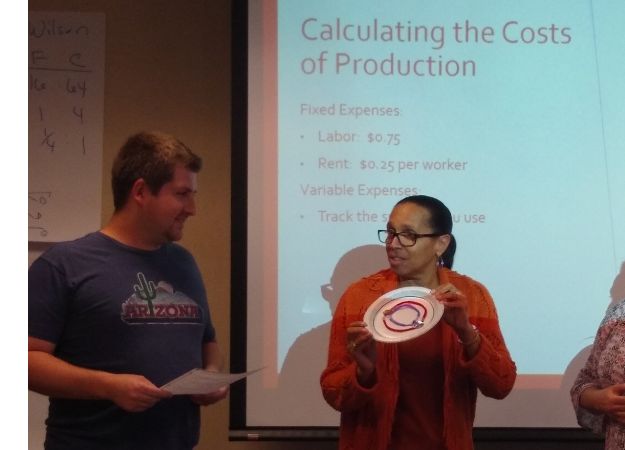 Teacher holding up a paper plate invention in front of the class.