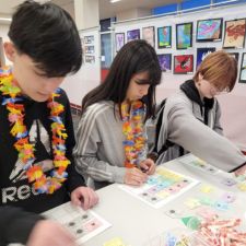 Three high school students wearing leis completing a financial literacy activity at a tall table. 