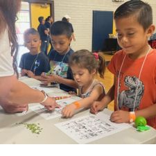 Four elementary students at a table completing a money counting activity with a volunteer in a school cafeteria.