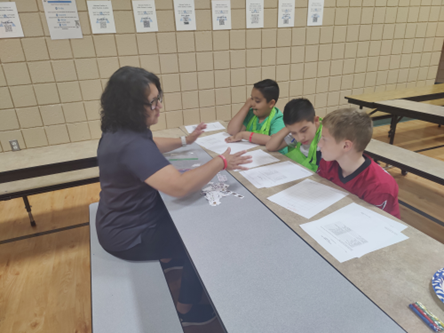 Volunteer Maria Echeveste doing an activity with students at a cafeteria table.